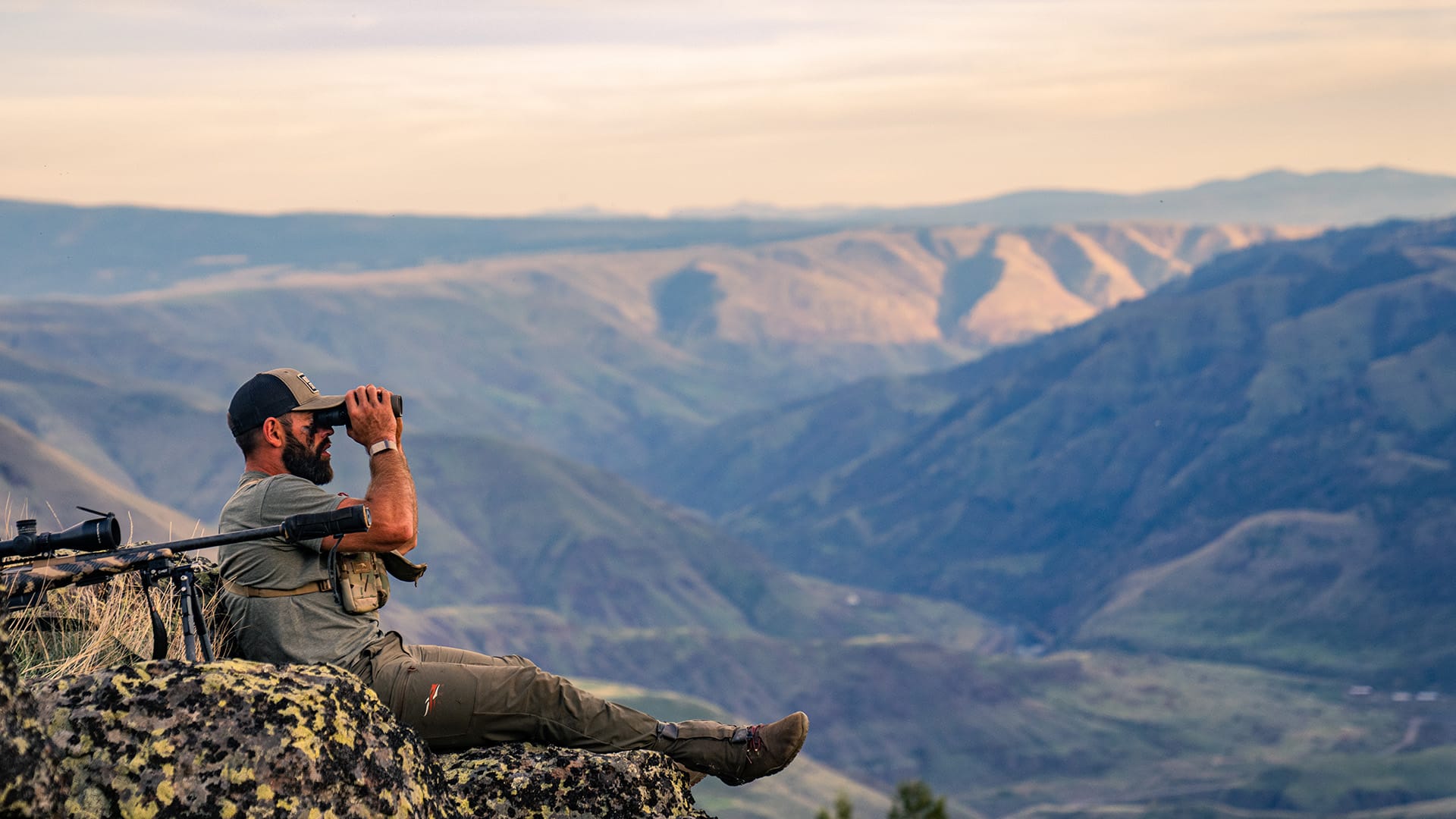 Rich Froning sitting on a mountain using binoculars
