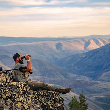 Rich Froning sitting on a mountain using binoculars
